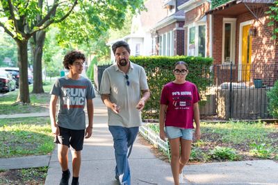 Pete Gonzales walking a residential District 3A sidewalk between two teenagers on a summer afternoon.