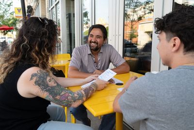 Pete Gonzales holding a campaign flyer at a cafe table with two neighbors.